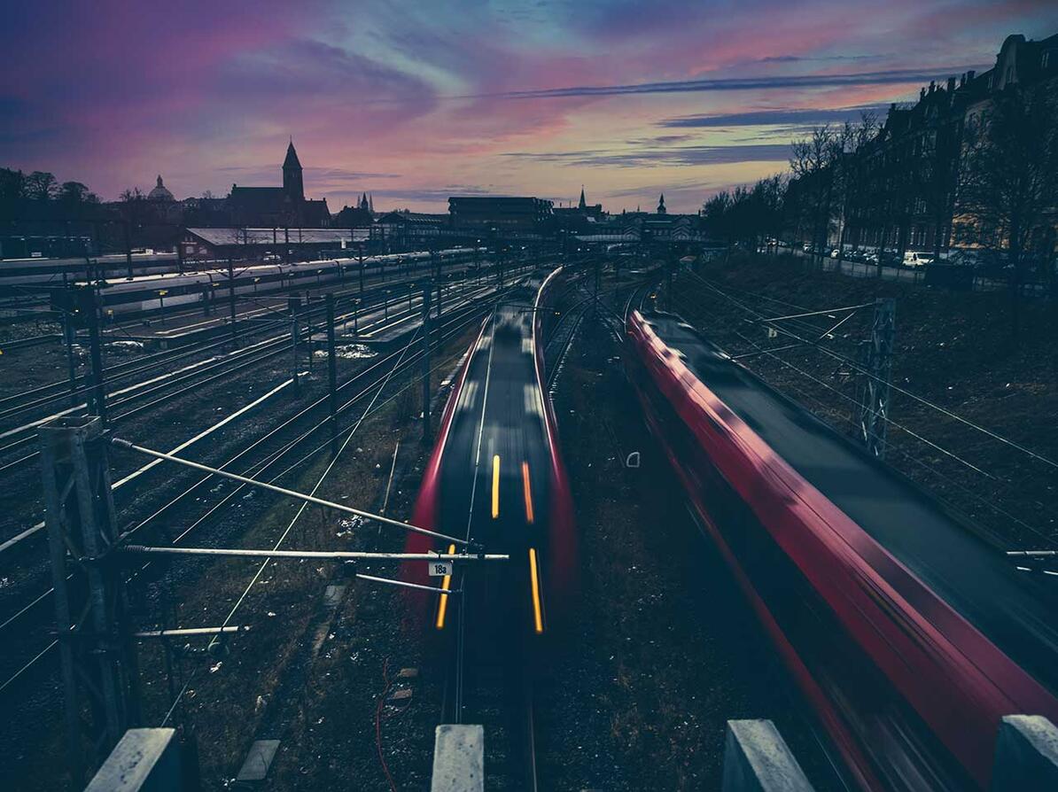 Røde tog kører på skinner under lyserød himmel