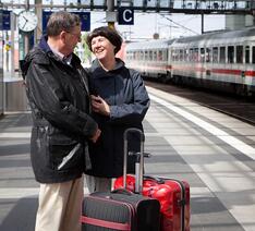 To glade ældre mennesker står på togperron