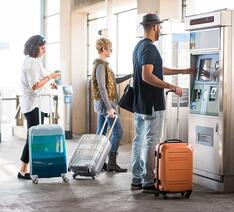 Mennesker med kufferter koeber billetter i billetautomat 