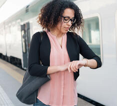 Kvinde står på togperron og kigger på sit ur