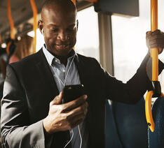 Mand står i bus og kigger på sin mobiltelefon